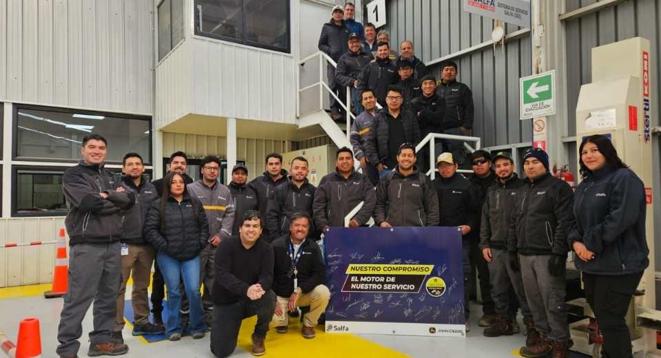 Equipo de técnicos y colaboradores de Salfa posando en taller junto a un banner de certificación Power Service de John Deere, celebrando el logro alcanzado en las sucursales de Calama y Concepción.